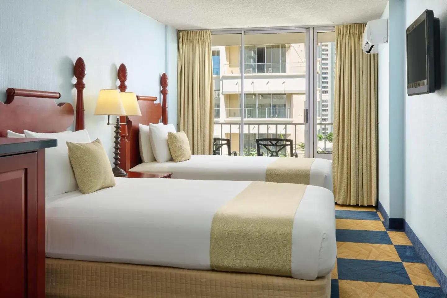 Guest room with two beds, balcony seating and wall TV at Ewa Hotel Waikiki.