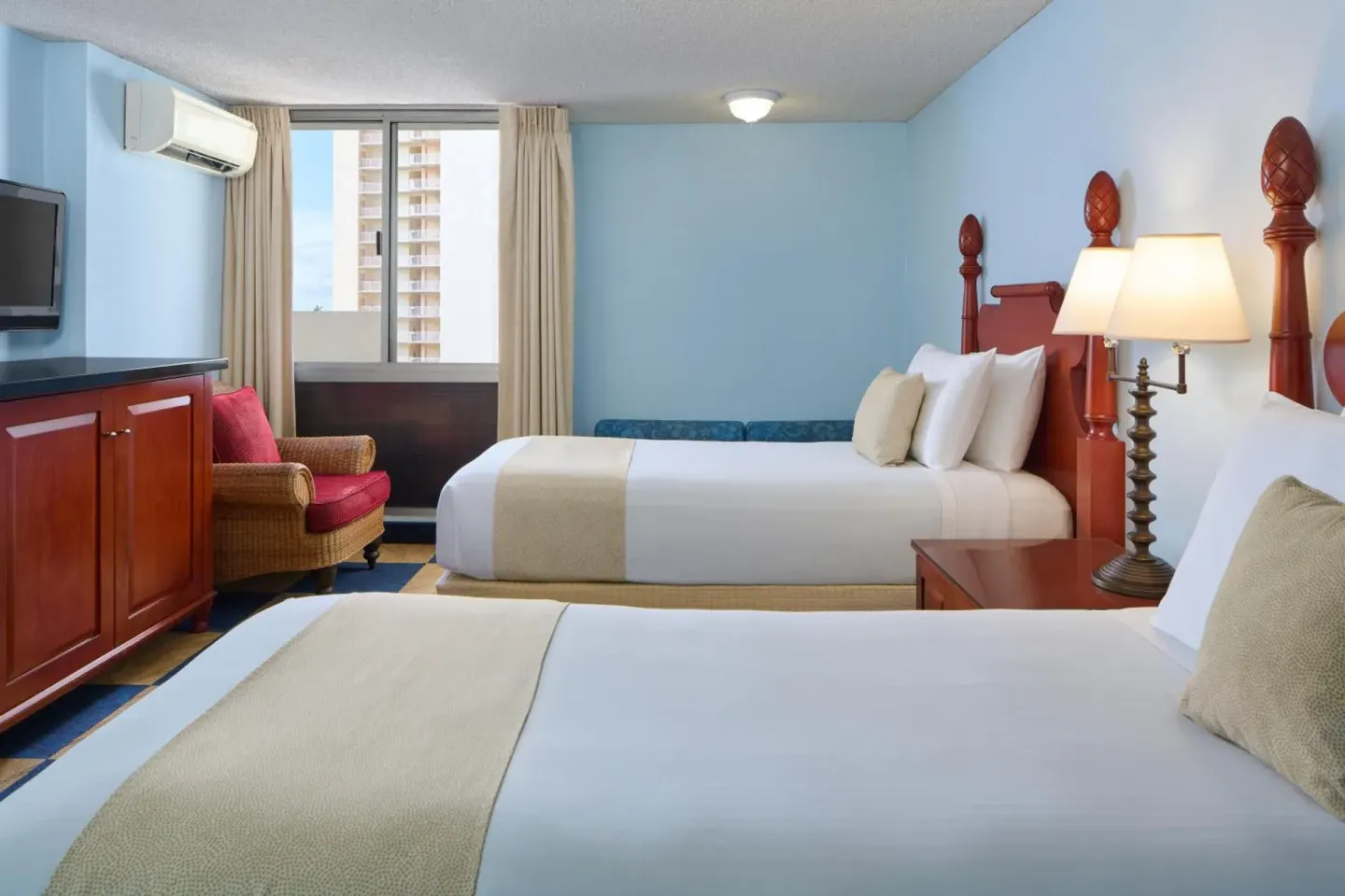 Two beds, a wicker chair, and blue walls in a guest room at Ewa Hotel Waikiki.
