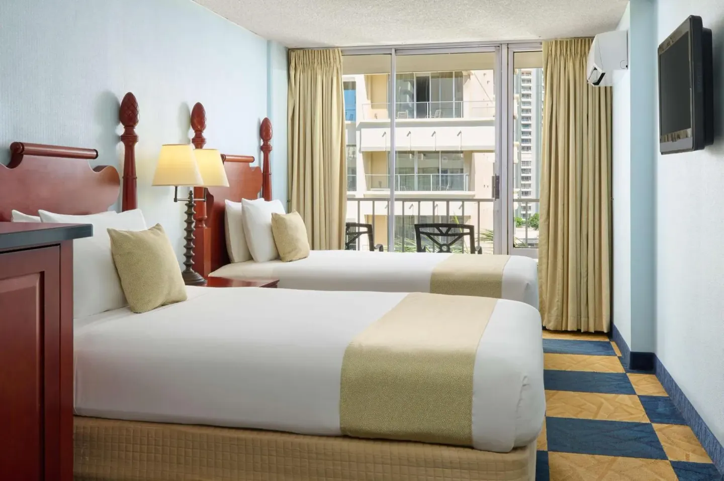 Two beds facing sliding balcony doors in a guest room at Ewa Hotel Waikiki.