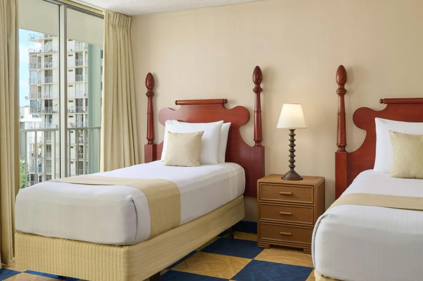 Two twin beds beside a window in a guest room at Ewa Hotel Waikiki.