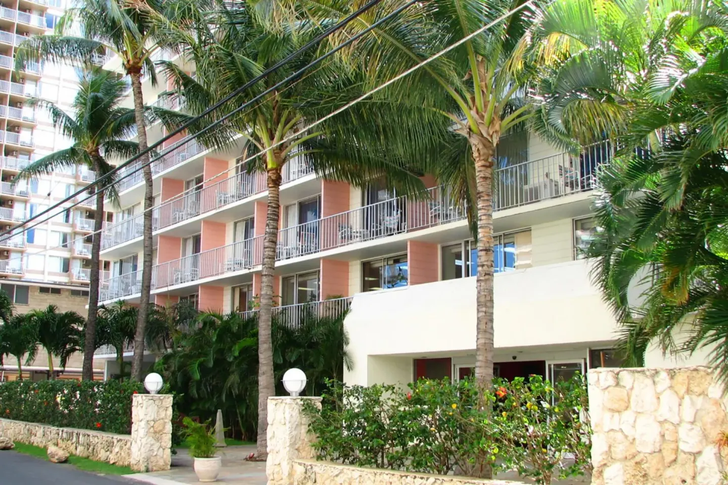 Palm-lined exterior with balconies and stone wall at Ewa Hotel Waikiki.