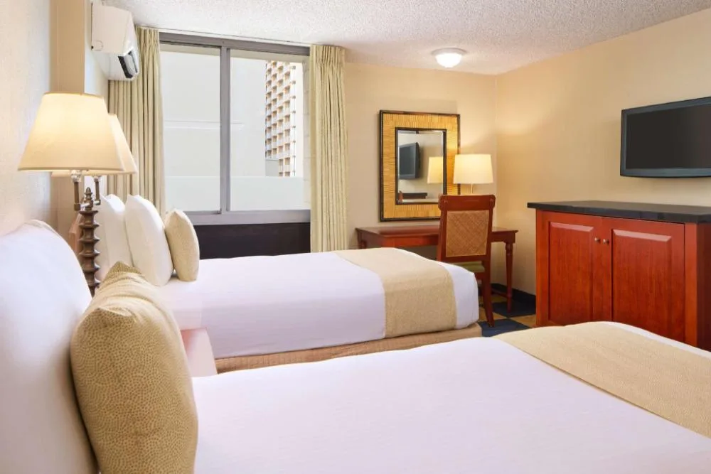 Moderate Room with two beds, desk, mirror and wall-mounted TV at Ewa Hotel Waikiki.