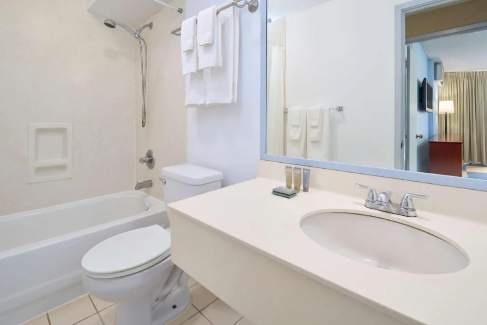 Bathroom vanity, tub shower, toilet, towels, and mirror in a suite at Ewa Hotel Waikiki.