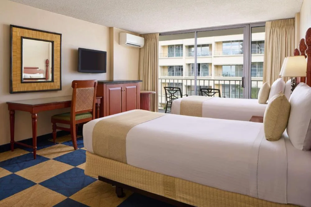 One Bedroom Suite with two beds, balcony seating, desk, and TV at Ewa Hotel Waikiki.