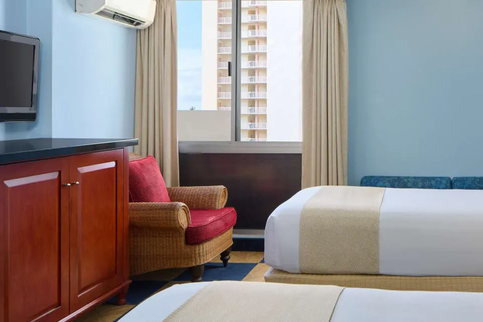 Studio kitchenette guest room corner with bed, TV cabinet, and chair at Ewa Hotel Waikiki.