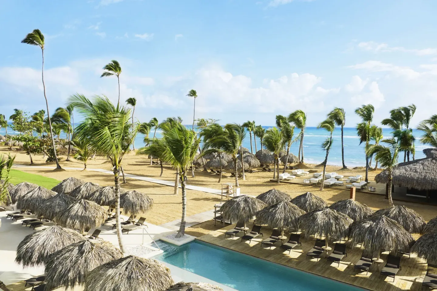Beach and pool area with thatched umbrellas and palms at Excellence El Carmen.