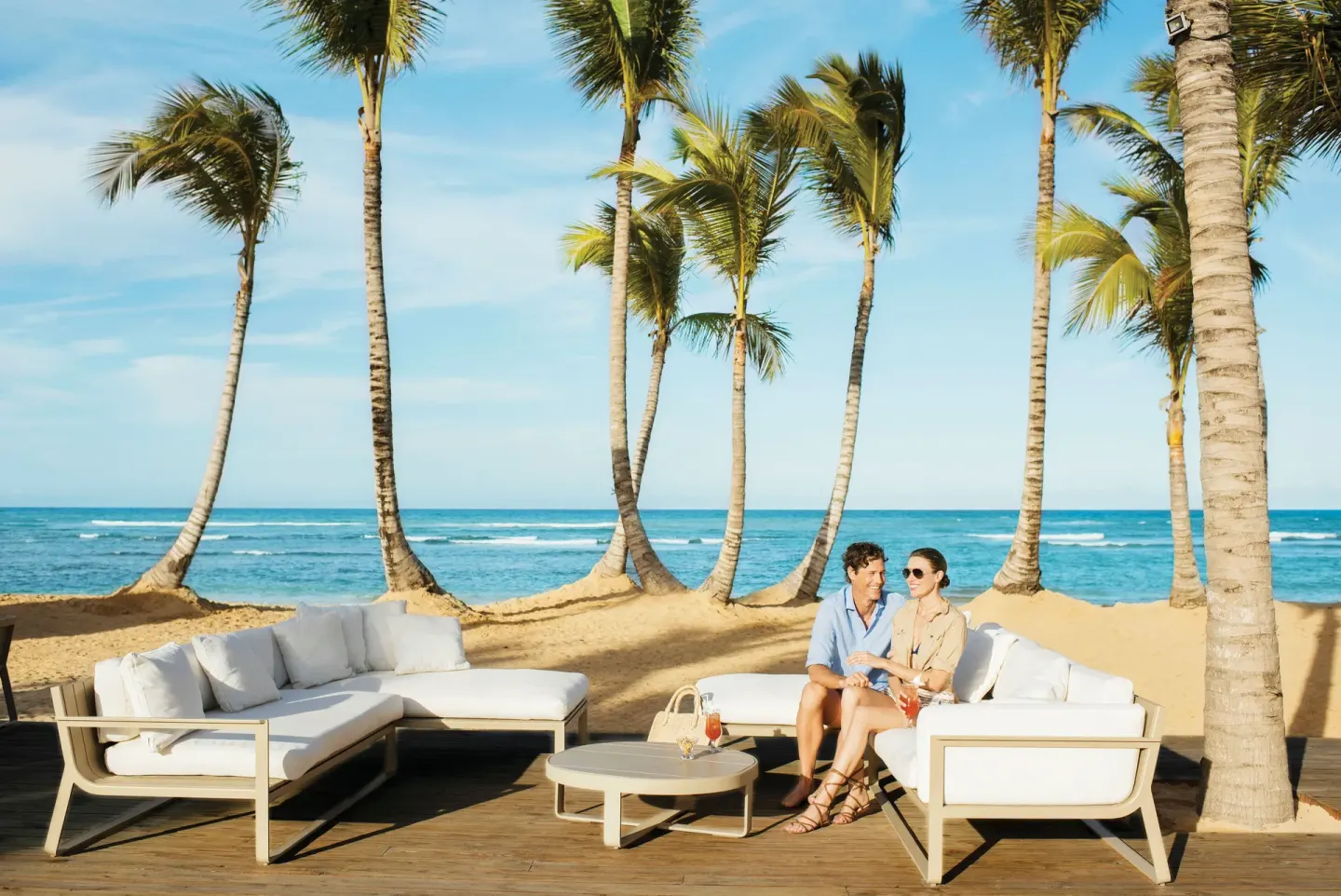 Couple seated on white beachfront lounge furniture by the ocean at Excellence El Carmen.