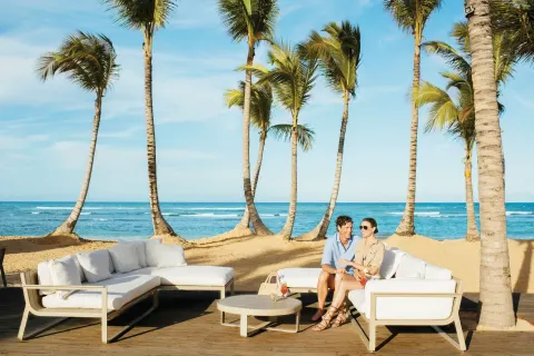Couple seated on white beachfront lounge furniture by the ocean at Excellence El Carmen.