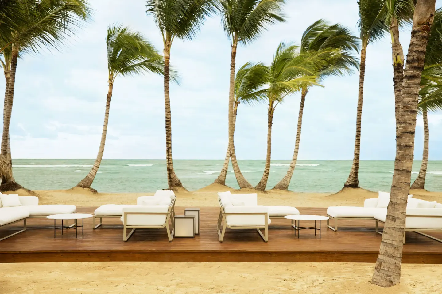 White outdoor lounge seating faces the ocean beneath palm trees at Excellence El Carmen.
