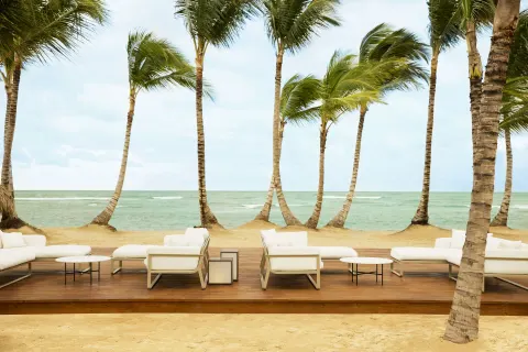 White outdoor lounge seating faces the ocean beneath palm trees at Excellence El Carmen.