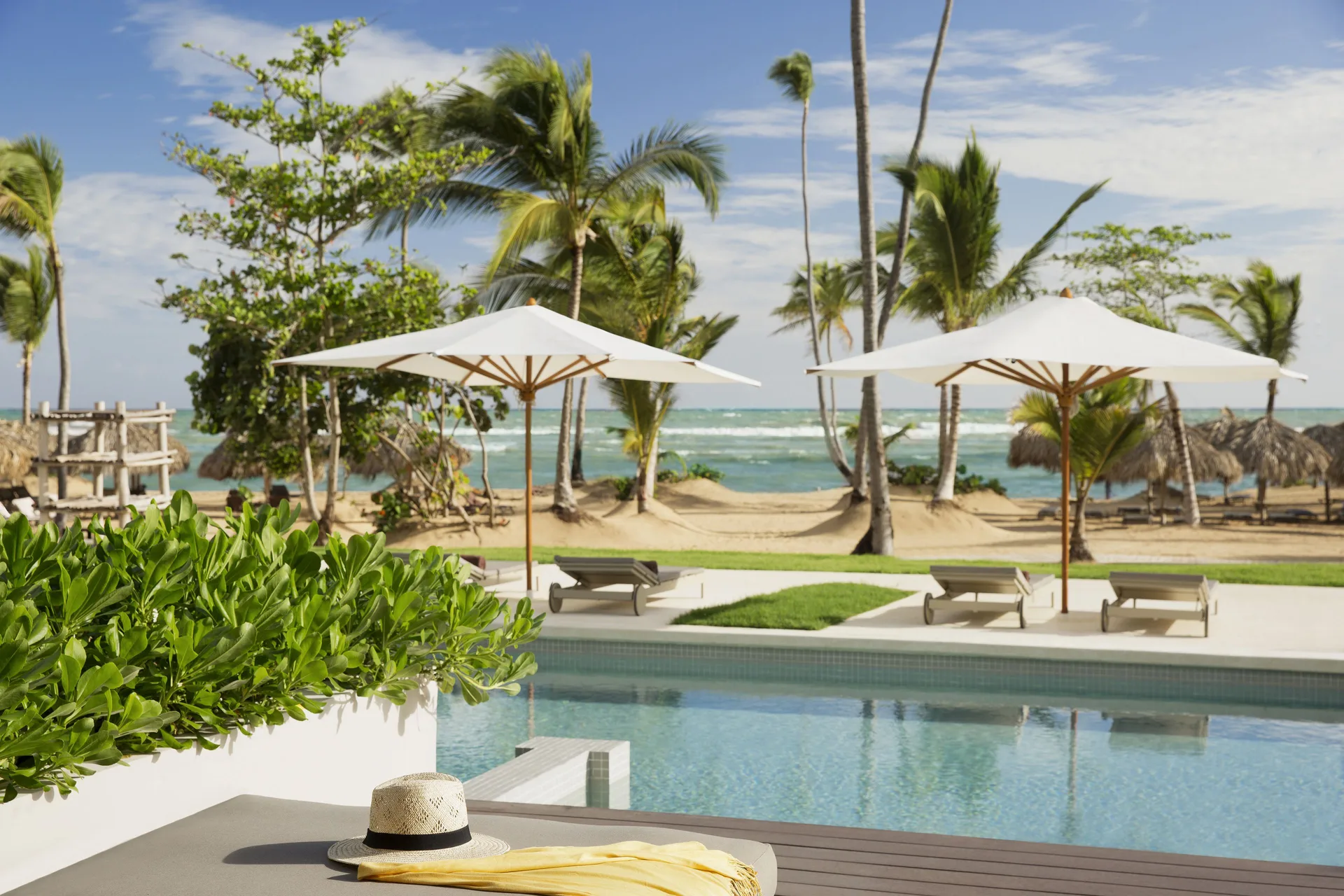 Beachfront pool with umbrellas and palm trees at Excellence El Carmen.