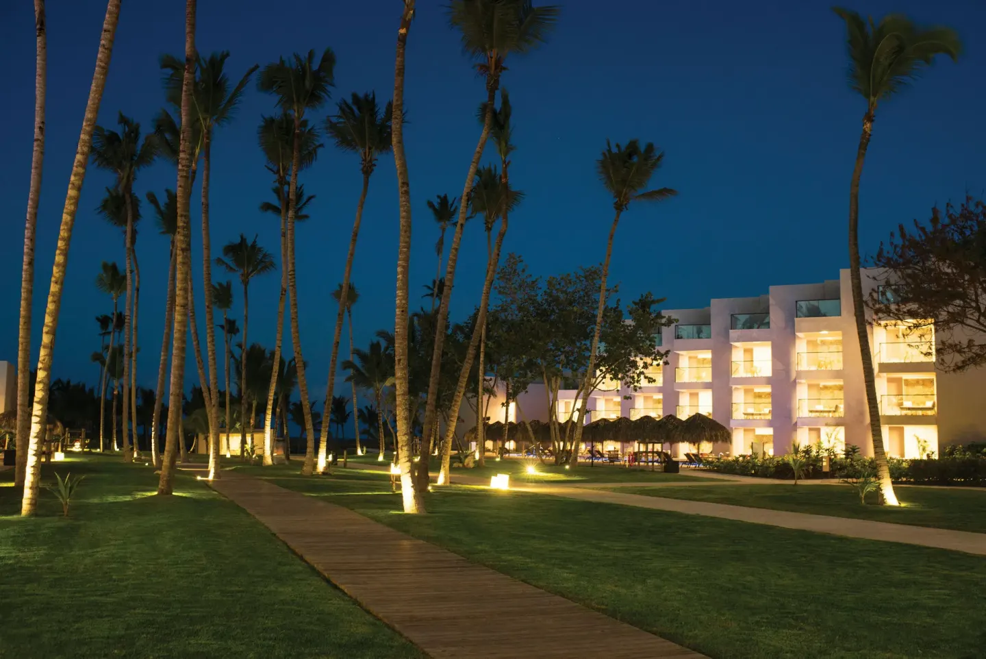 Illuminated palm-lined resort walkway and guest buildings at Excellence El Carmen.