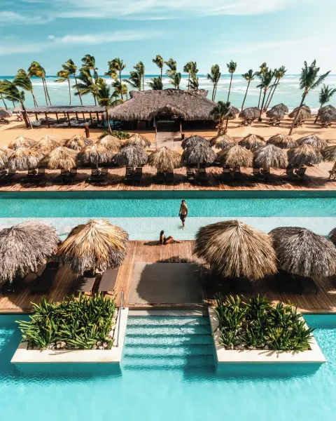 Pool, palapa shade, beachfront pavilion, palms, and ocean at Excellence El Carmen.
