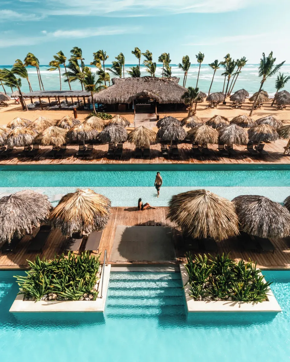 Pool, palapa shade, beachfront pavilion, palms, and ocean at Excellence El Carmen.
