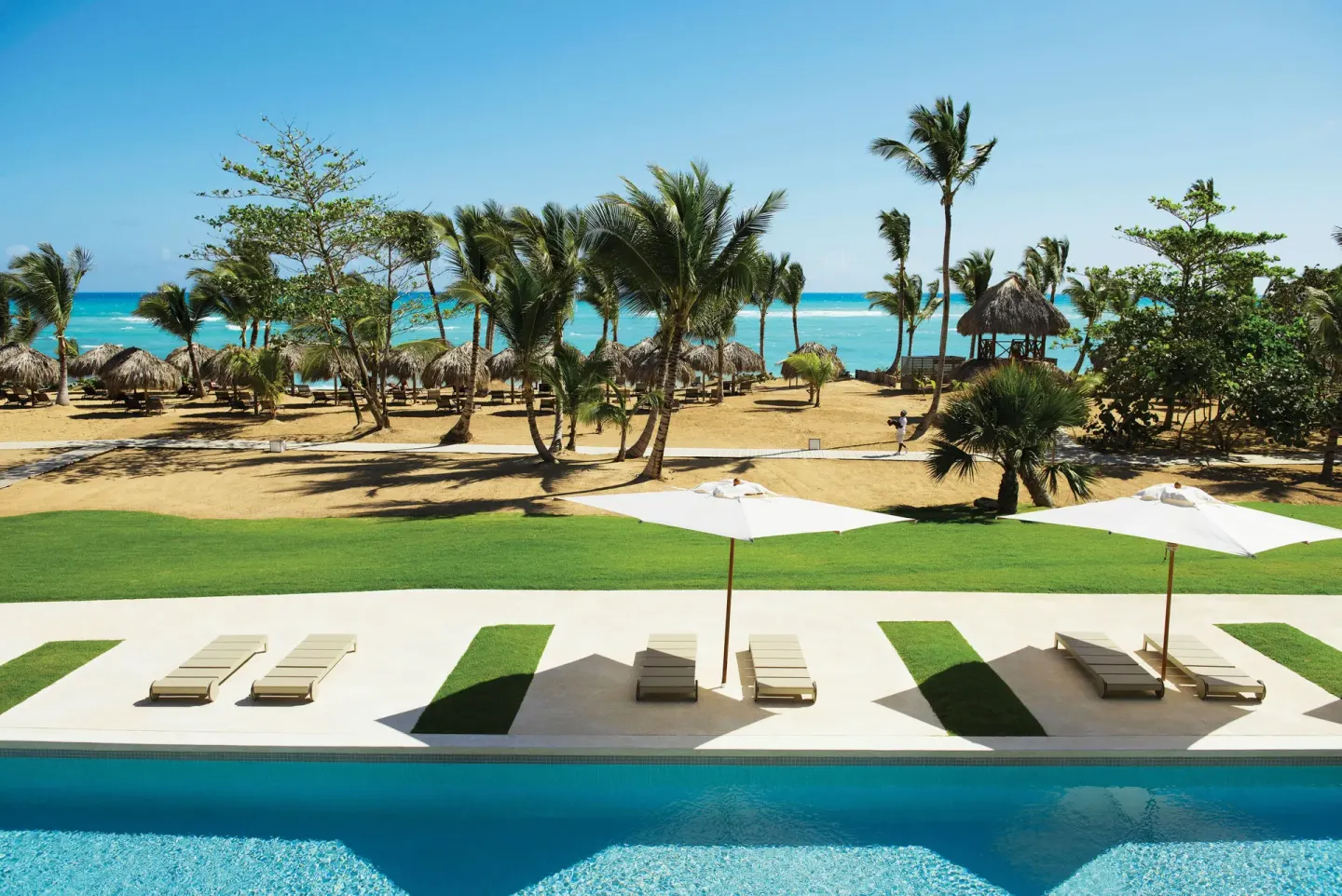 Poolside loungers and umbrellas facing the palm-lined beach at Excellence El Carmen.