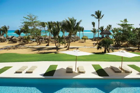 Poolside loungers and umbrellas facing the palm-lined beach at Excellence El Carmen.
