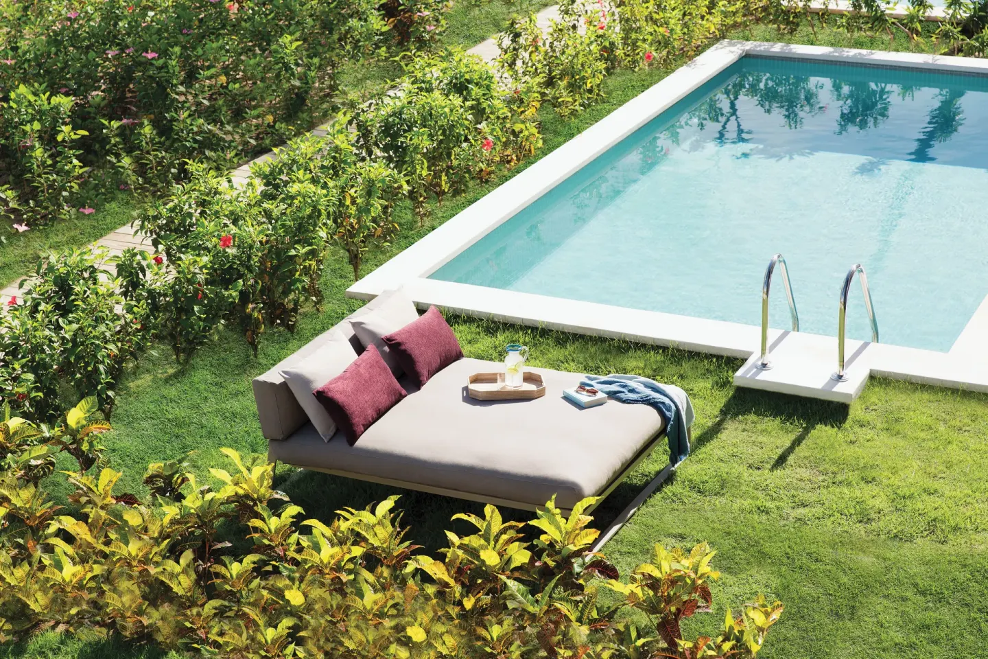 Private pool patio with daybed, pillows, and garden hedges at Excellence El Carmen.