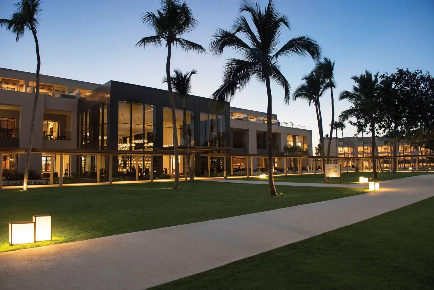 Resort buildings, palm trees, lawns, and lit pathways at dusk at Excellence El Carmen.