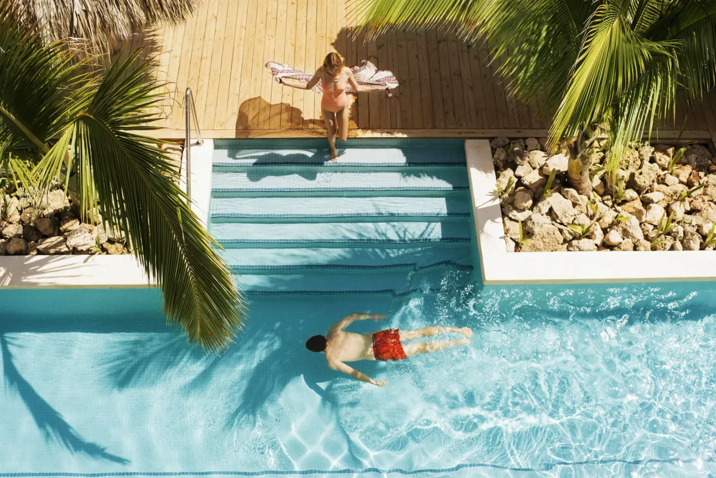 Overhead view of guests at a pool with palms and wooden deck at Excellence El Carmen.