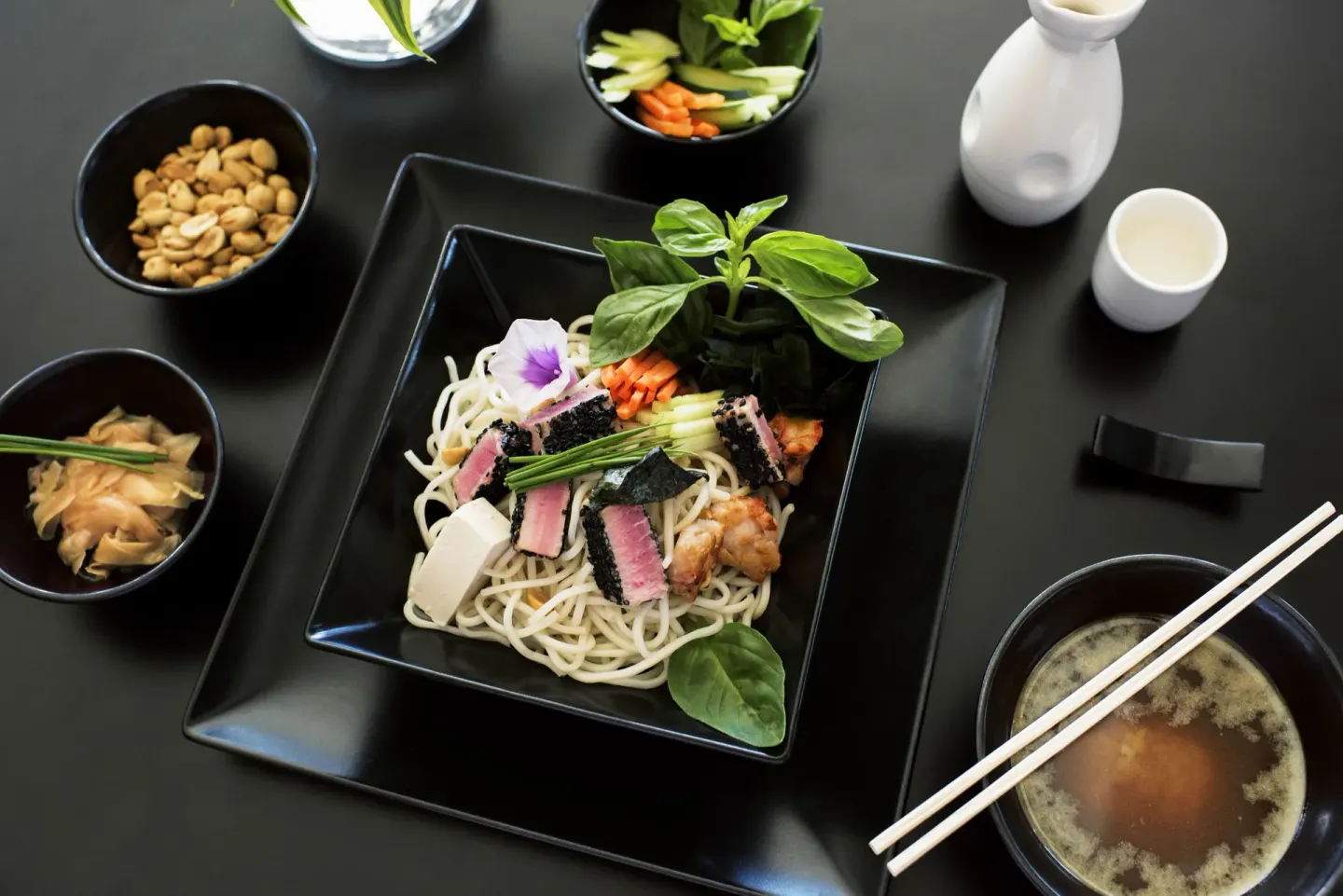 An Asian-style noodle dish with soup, chopsticks, and side bowls at Excellence El Carmen.