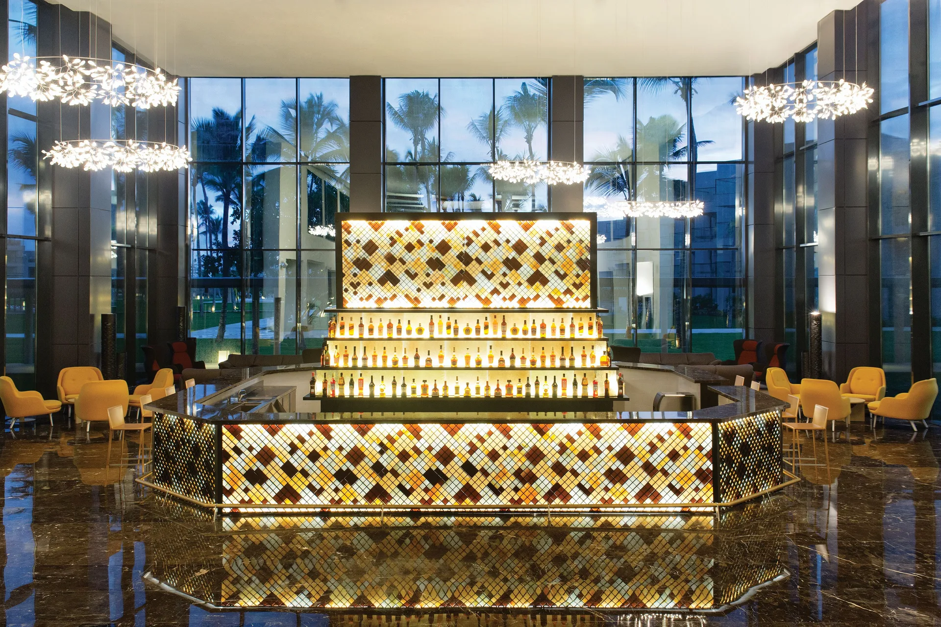 A dramatic illuminated lobby bar with tall windows and chandeliers at Excellence El Carmen.