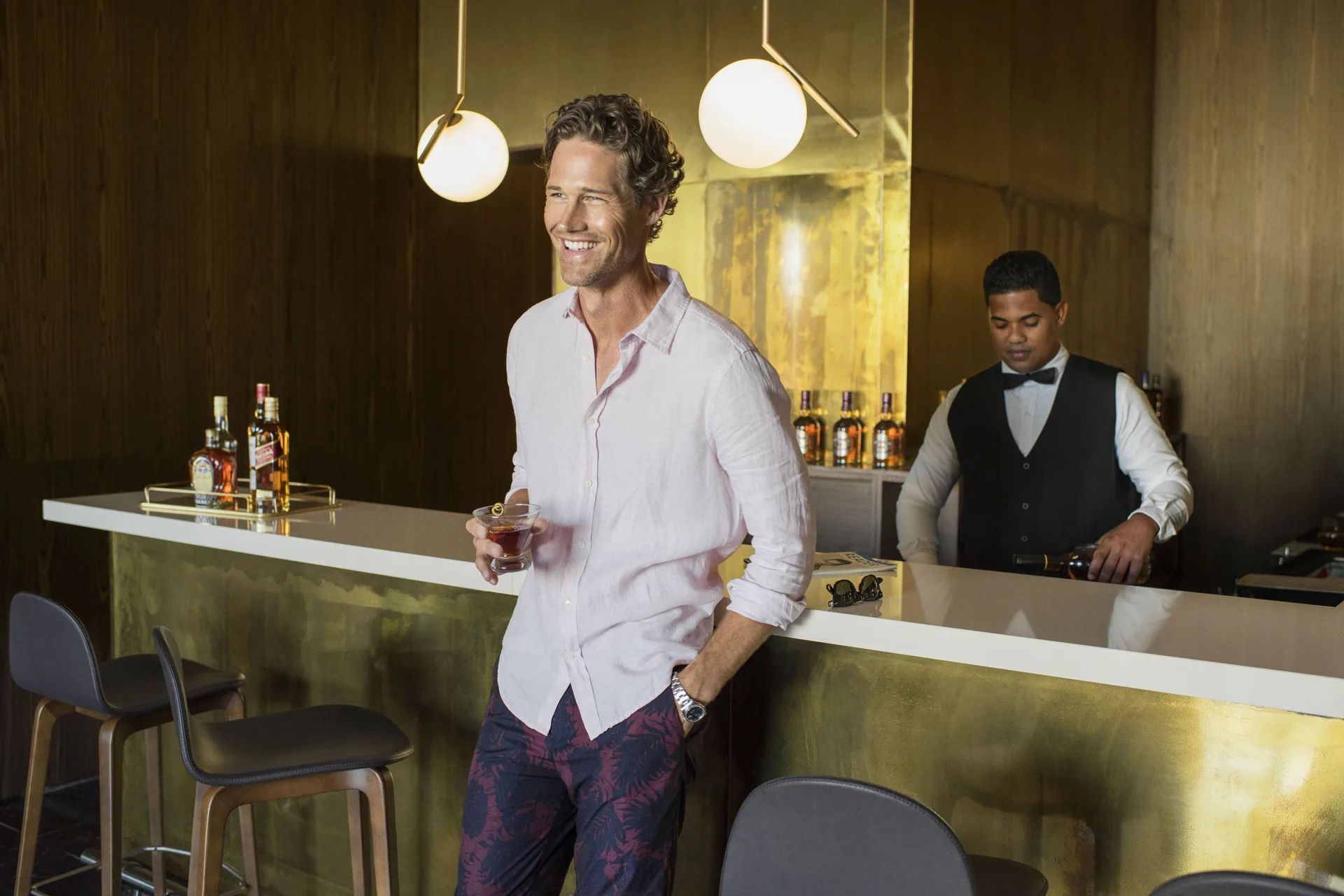 A guest holds a drink at a gold-toned bar at Excellence El Carmen.