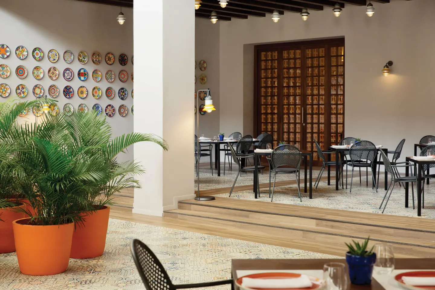A patio-style restaurant with decorative plates and potted palms at Excellence El Carmen.