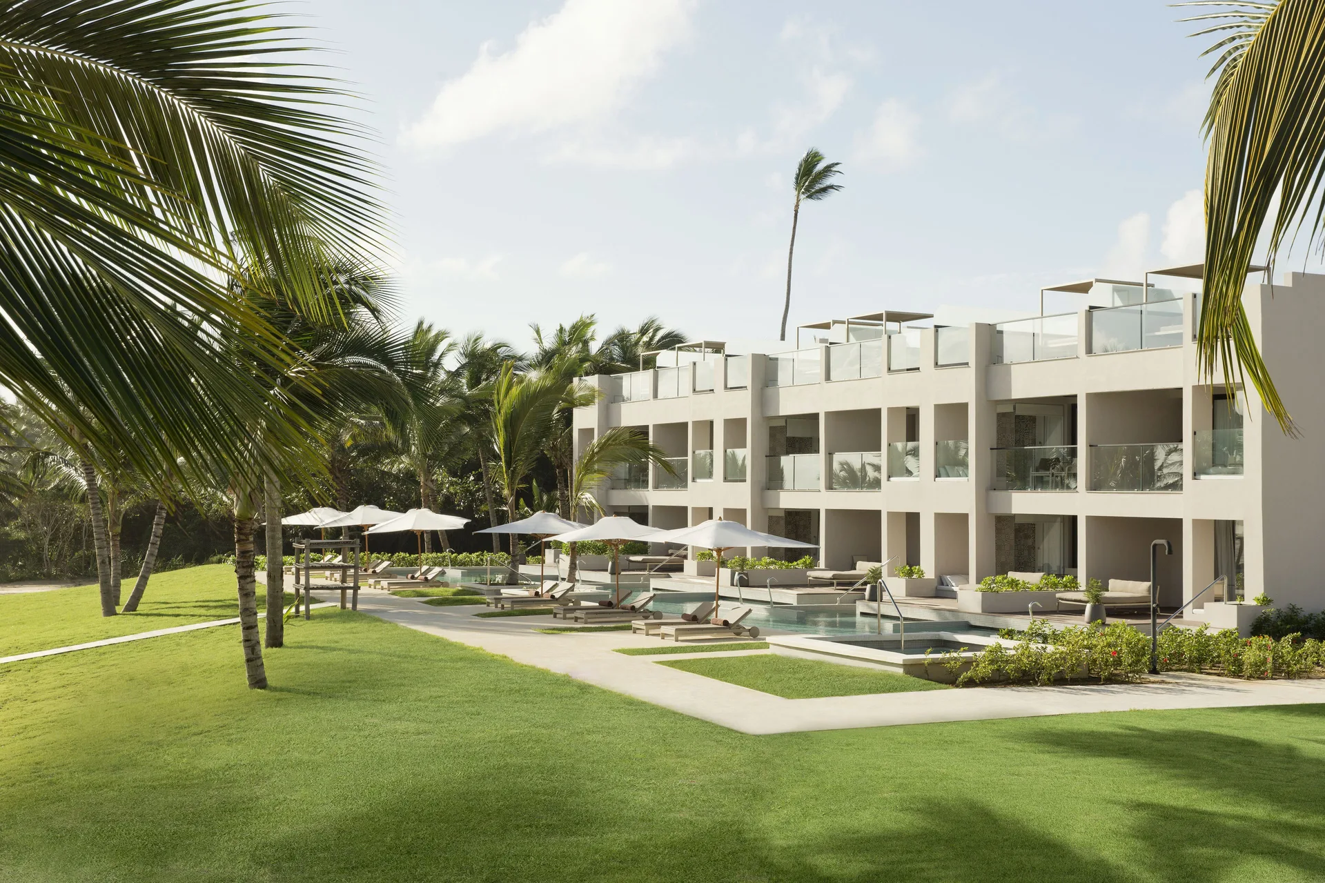 Beachfront swim-up suite building with pools, lawns, and palms at Excellence El Carmen.