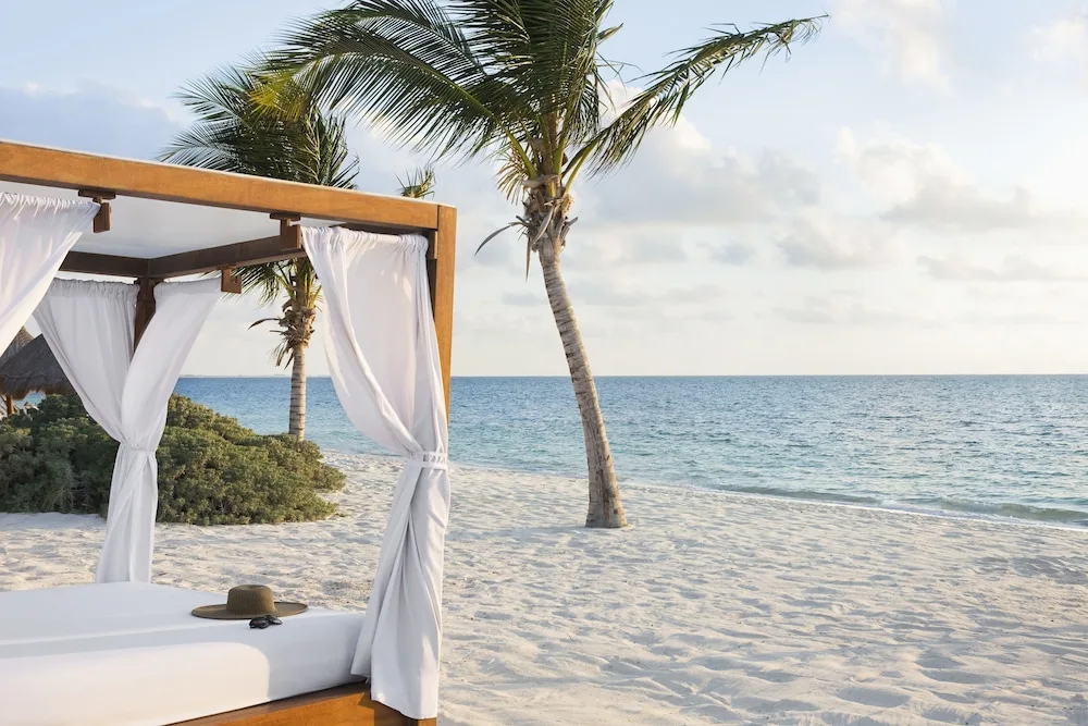 Beach cabana with white curtains beside the ocean at Excellence Playa Mujeres.