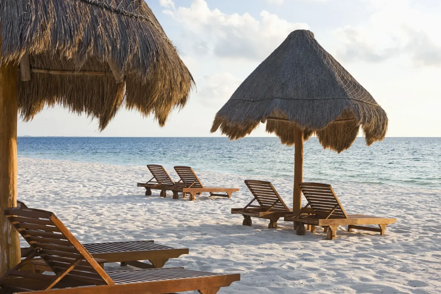 Wooden loungers under thatched palapas on the beach at Excellence Playa Mujeres.