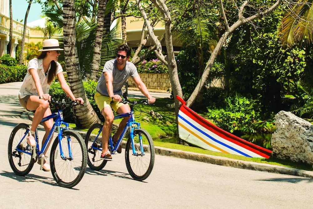 Guests riding bicycles along a tropical path at Excellence Playa Mujeres.