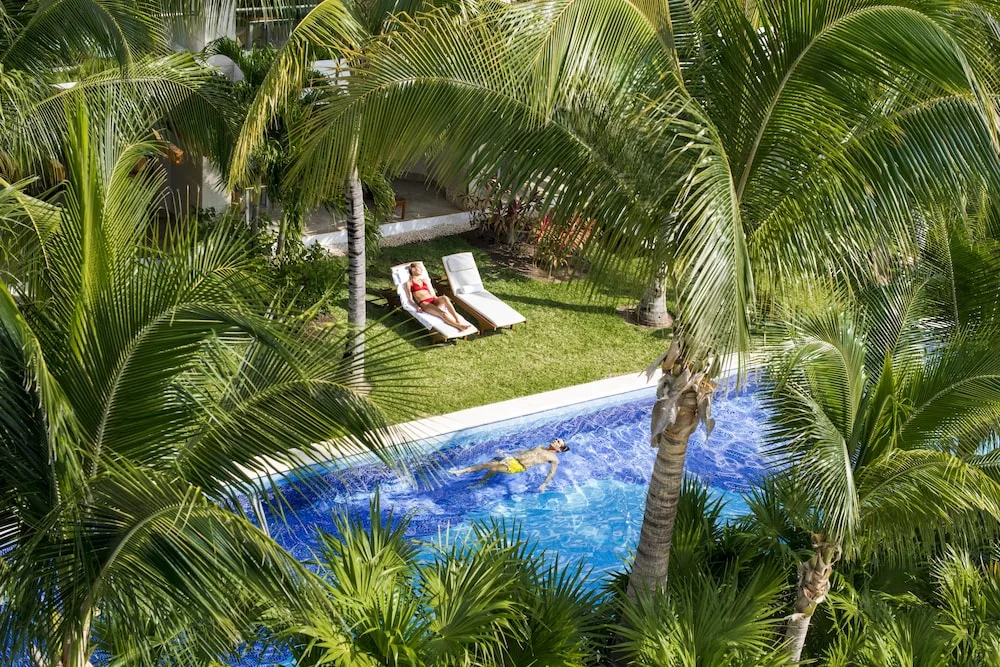 Guests relaxing by a narrow pool among palms at Excellence Playa Mujeres.