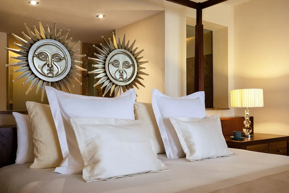 Guest room bed with white pillows and sunburst wall art at Excellence Playa Mujeres.