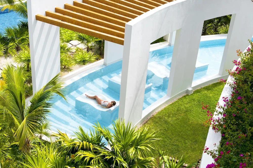 Guest reclining on an in-pool lounger framed by white arches at Excellence Playa Mujeres.