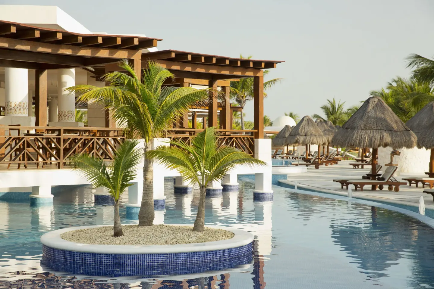 Poolside palms, lounge chairs and thatched umbrellas at Excellence Playa Mujeres.