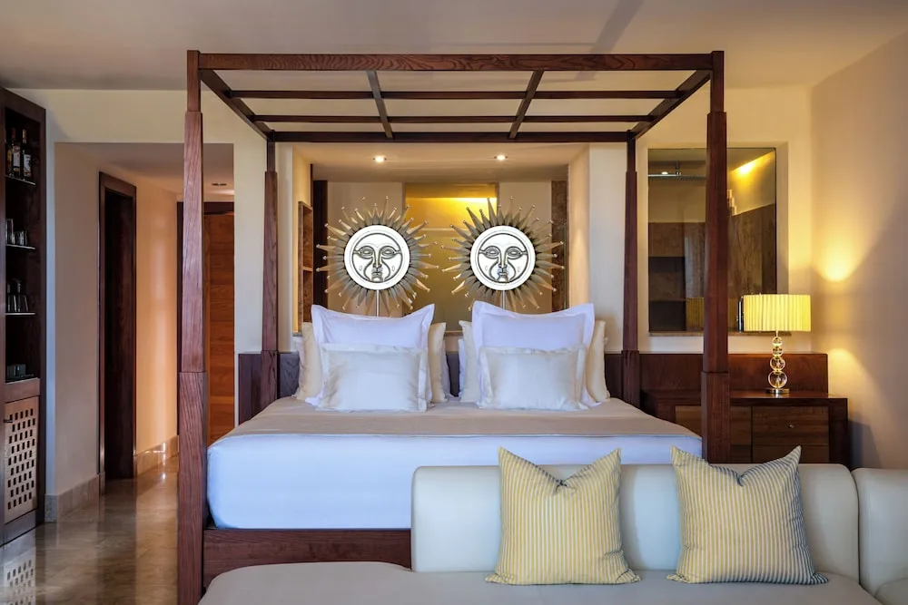 Suite bedroom with a four-poster king bed and sofa at Excellence Playa Mujeres.