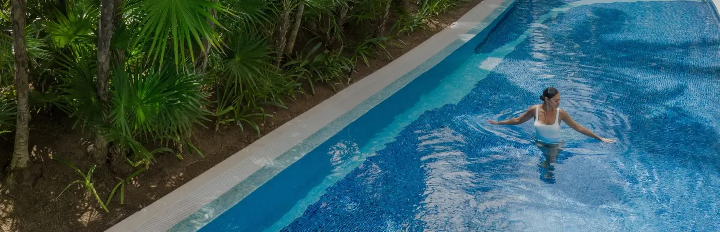 Guest wading in a blue pool bordered by tropical plants at Excellence Playa Mujeres.