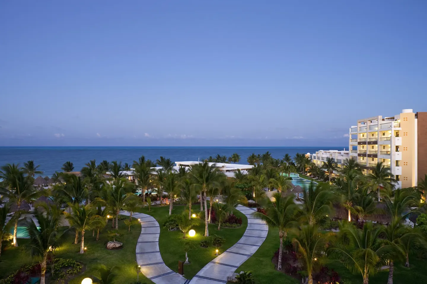 Twilight view of gardens, paths, and oceanfront buildings at Excellence Playa Mujeres.