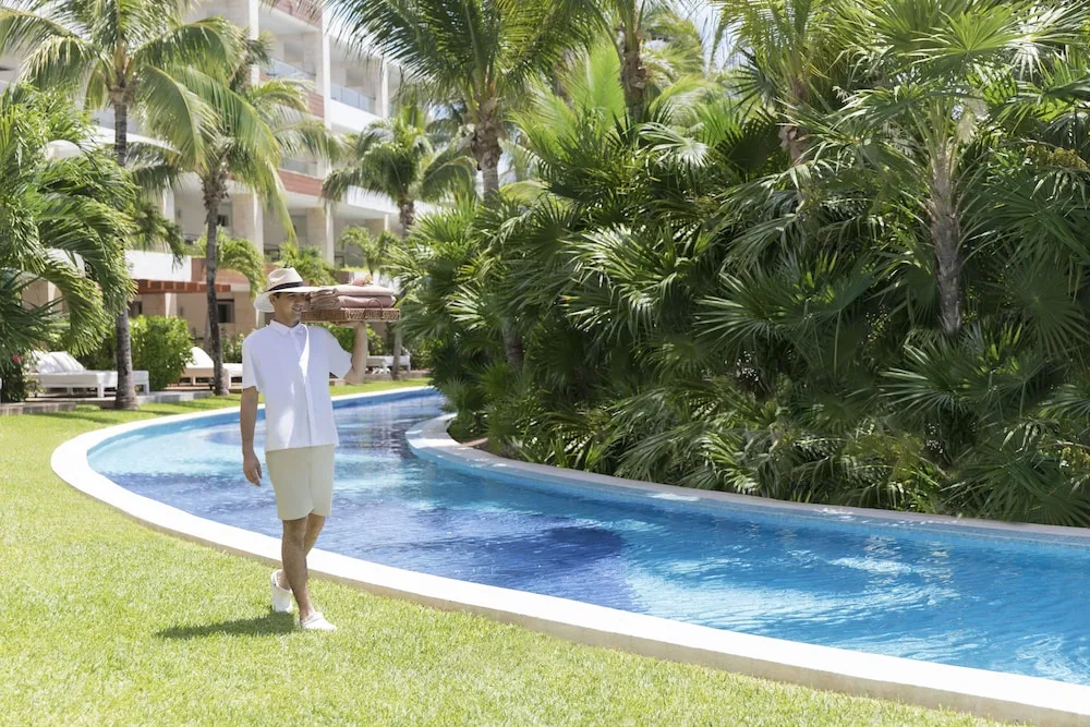 A staff member carries towels beside a winding pool at Excellence Playa Mujeres.