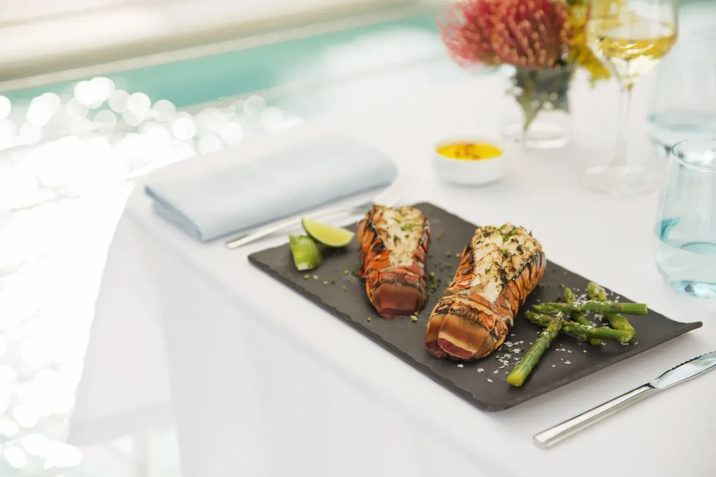 Grilled lobster tails with asparagus are plated by the water at Excellence Playa Mujeres.