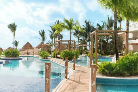 Pool view with wooden bridge and palm trees at Excellence Playa Mujeres.