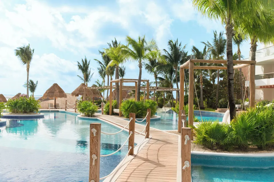 Pool view with wooden bridge and palm trees at Excellence Playa Mujeres.