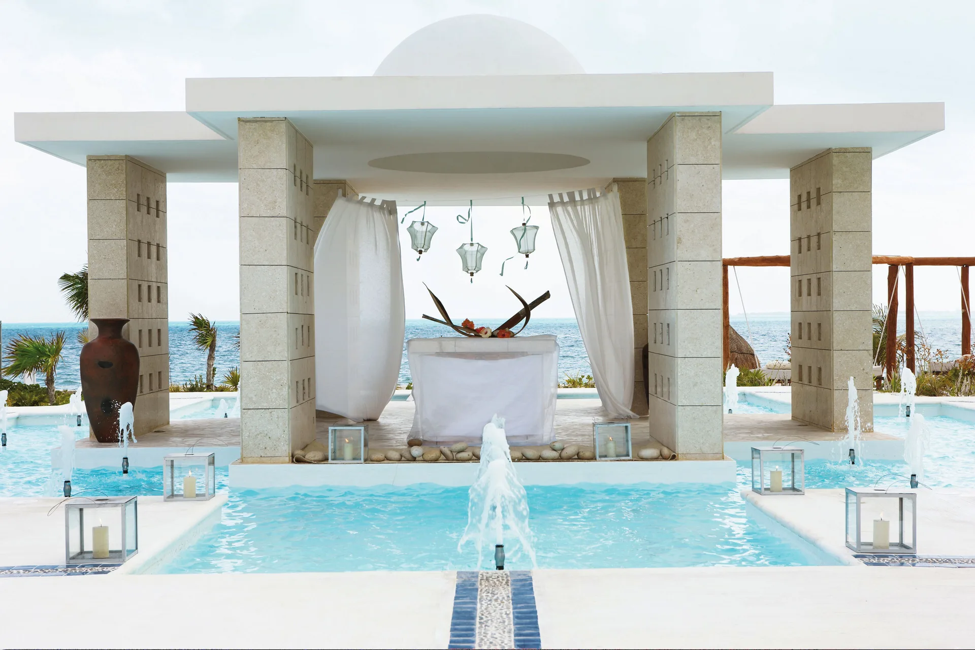 Poolside wedding altar with fountains, curtains, lanterns, and ocean view at Excellence Playa Mujeres.