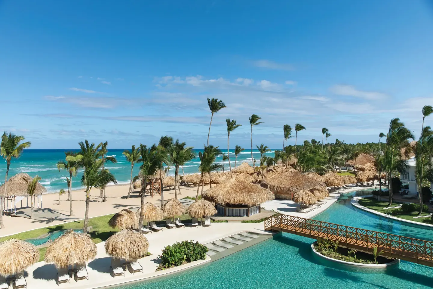 Resort pool, beach palapas, palms, and ocean at Excellence Punta Cana.