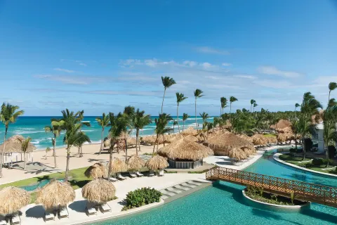 Resort pool, beach palapas, palms, and ocean at Excellence Punta Cana.