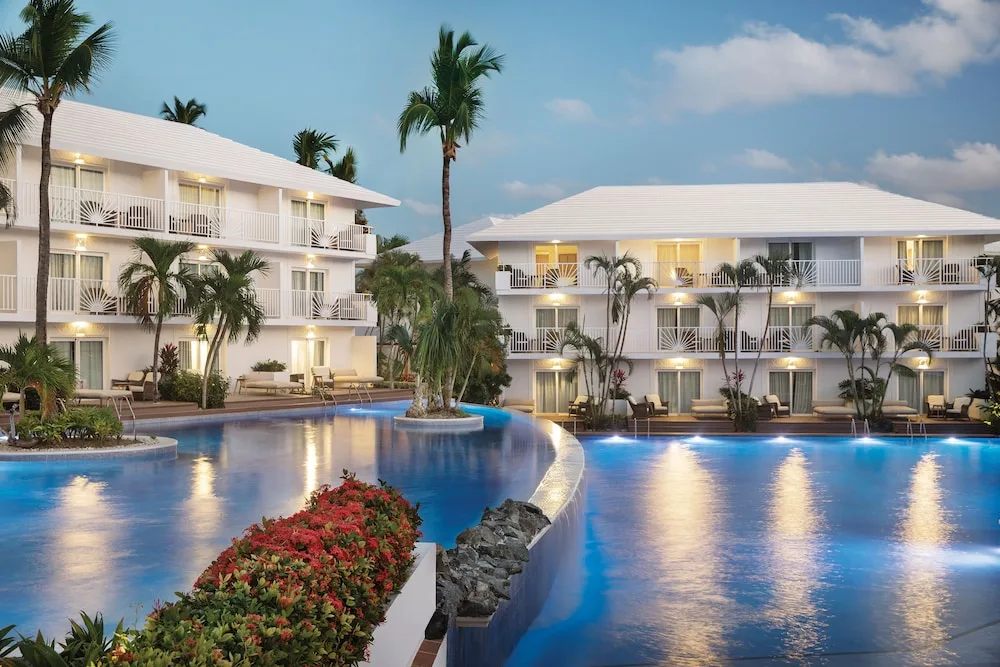 Evening pool bordered by white guest-room buildings at Excellence Punta Cana.