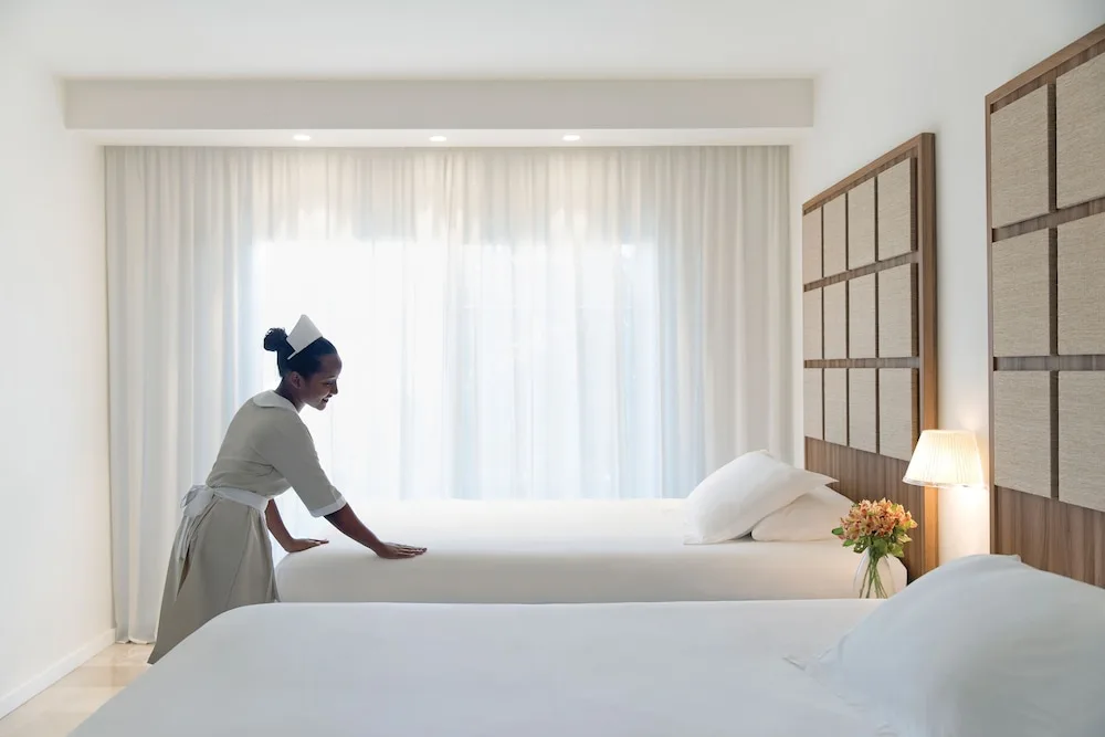 A housekeeper smooths one of two white beds in a room at Excellence Punta Cana.