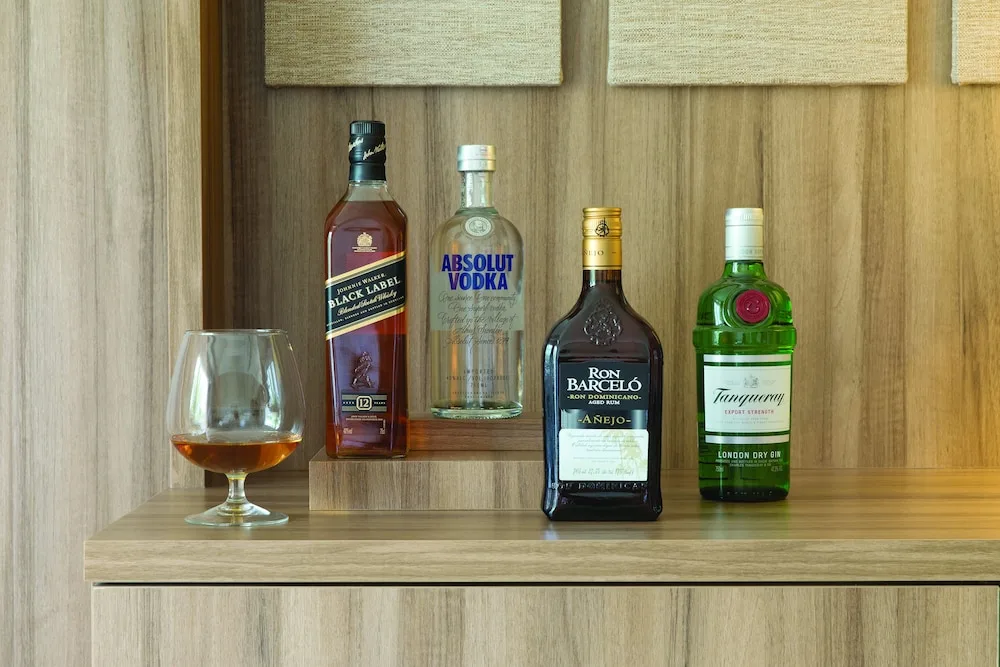 In-room liquor bottles and a glass on a wooden cabinet at Excellence Punta Cana.
