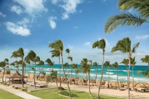 Palm-lined beach with palapas and turquoise surf at Excellence Punta Cana.