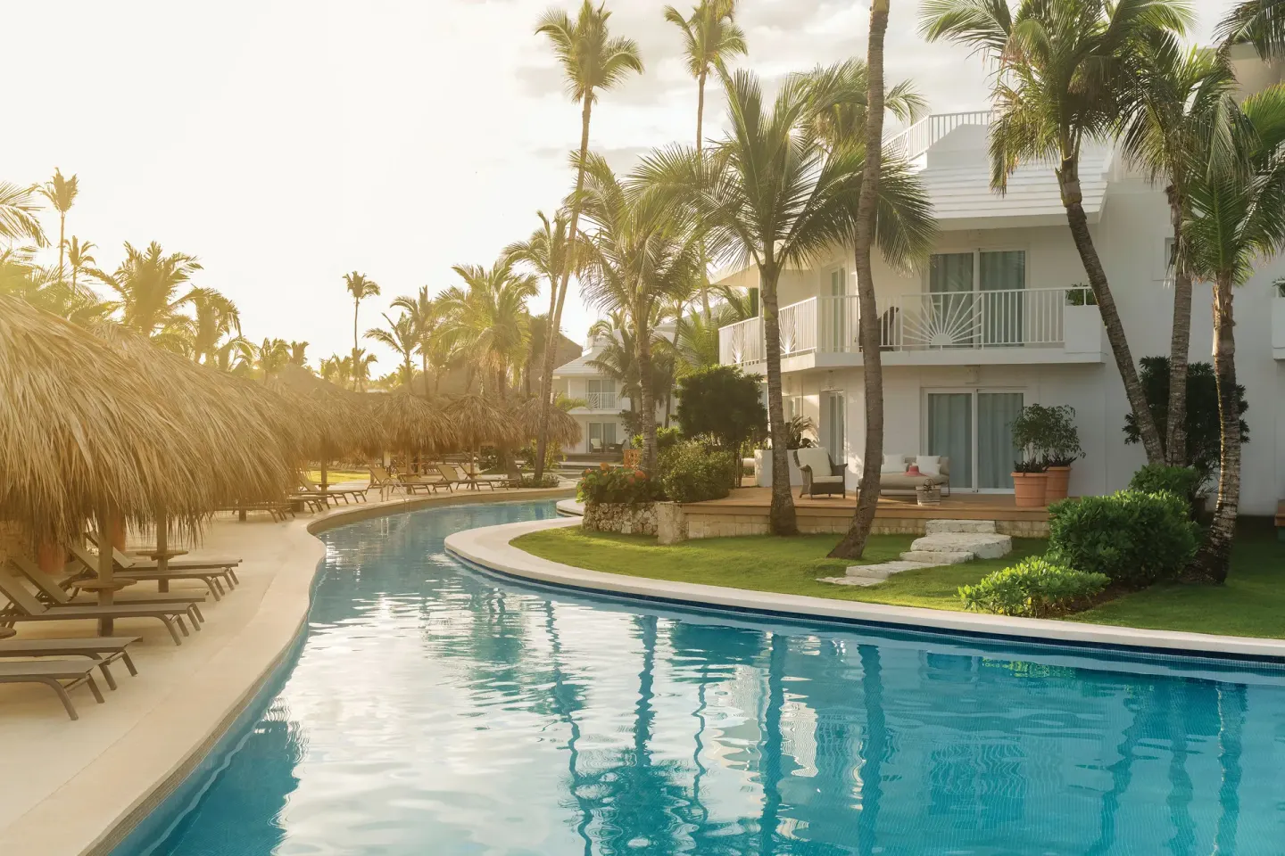 Curving pool beside white guest buildings and palms at Excellence Punta Cana.